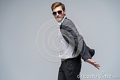 Feeling free and comfortable in his style. Handsome young man in full suit and sunglasses moving in front of gray Stock Photo