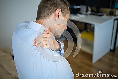 Feeling tired. Back view of frustrated young man looking exhausted and massaging his neck while sitting at workplace Stock Photo