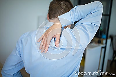 Feeling tired. Back view of frustrated young man looking exhausted and massaging his neck while sitting at workplace Stock Photo