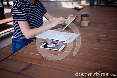 Feemale reelancer, with large wrist watch, works at a wooden table on tablet, with gadgets and papers. Stock Photo