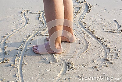 Feet of a boy is painting figures in the fine sand Stock Photo