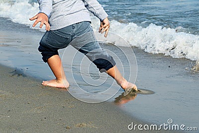 Feet of the boy in wet gray jeans escaping from the wave on sandy beach Stock Photo