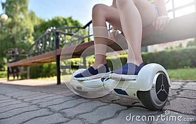 Feet of a girl child on a hoverboard while relaxing on a bench in a park Stock Photo