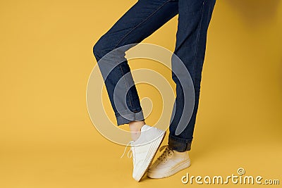 feet jeans fashion shoes white sneakers yellow background Stock Photo