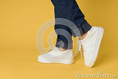 feet jeans fashion shoes white sneakers yellow background Stock Photo