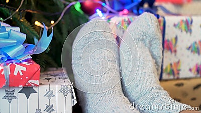 Feet in knitted socks near New Year presents on Christmas tree background, winter holidays and home comfort concept Stock Photo