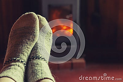 Feet legs in winter clothes wool socks at fireplace background. Woman sitting at home on winter or autumn evening relaxing and Stock Photo