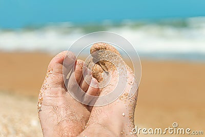 Feet of a man lying on the beach. Vacationer relaxes near the azure sea at sunny day. Stock Photo