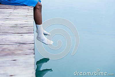 Feet of a man in white socks hanging over water at the dock Stock Photo