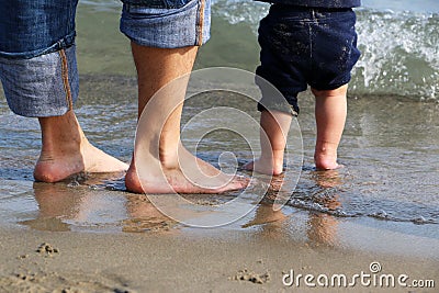 Feet of the men and baby standing in shallow water waiting for the wave Stock Photo