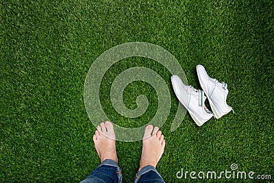 Feet resting on green grass with lying sneakers Stock Photo