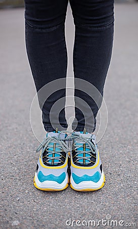 Feet shod in sneakers multi-colored yellow, white, black and blue are on the asphalt road. Stock Photo