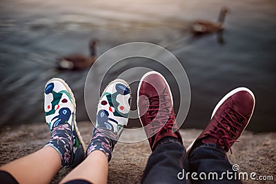 Feet with shoes of the couple on romantic date sitting on the rocks near lake Stock Photo