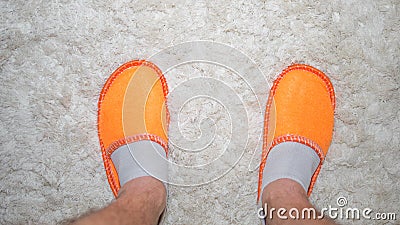 Feet in slippers on a white rug,cozy home furnishings,men`s feet in orange slipper,top view.Home lifestyle. Stock Photo