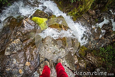 The feet of a tourist stand on a rock above a mountain waterfall. Shevelev. Stock Photo