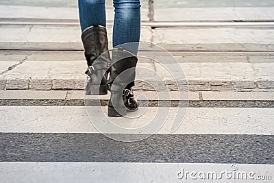 Feet of a woman with boots walking on the white strips of a pedestrian zebra crossing, or crosswalk, to pass a street and road use Stock Photo