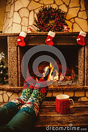 Feet in woollen socks by the Christmas fireplace. Woman relaxes Stock Photo