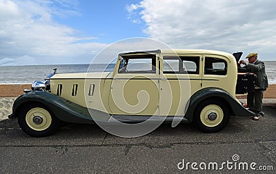 Beautiful Cream Coloured Classic Rolls Royce Motor Car parked on seafront promenade with man operating gramophone, beach and sea i Editorial Stock Photo