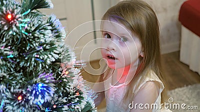 Feliz bebé está jugando cerca del árbol de Navidad y sonriendo La chica le acarició un hermoso abeto peludo Inteligente almacen de metraje de vídeo Feliz bebé está jugando cerca del árbol de Navidad y sonriendo La chica le acarició un hermoso abeto peludo Inteligente almacen de metraje de vídeo
