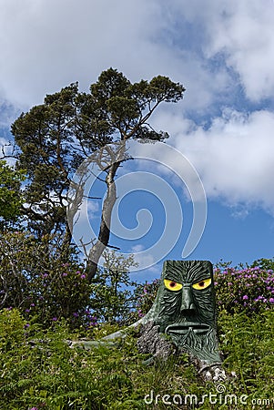 A Felled Tree Stump carved in the shape of a Forest Monster with Yellow eyes in the undergrowth of the Lews Castle Walk Editorial Stock Photo