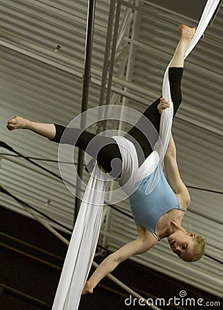 A female acrobat hangs upside down by wrapping aerial silks around her waist and legs. Editorial Stock Photo