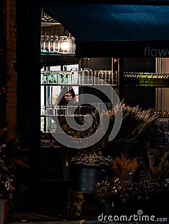 Female adult standing in a flower shop illuminated by the lights of the night Editorial Stock Photo