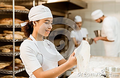 female african american baker kneading dough at baking manufacture while her colleagues working blurred Stock Photo