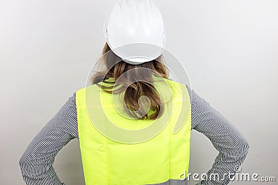 Female architect wearing reflecting jacket and hardhat standing backwards with hands on hips looking up. Stock Photo