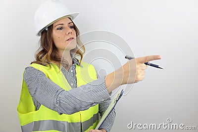 Female architect wearing work helmet and reflecting jacket, holding flip board and pointing with finger to side. Stock Photo