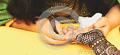 A female artist performing mehandi or henna design on female hand Stock Photo