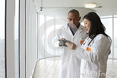 Female Asian doctor talking with African American doctor with tablet Stock Photo