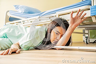 Female asian patient fell lying on the floor at hospital. She is trying to raise their hand and ask for help, Stock Photo