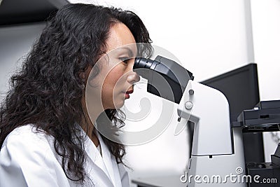 Female Asian scientist looking into eyepieces of microscope Stock Photo