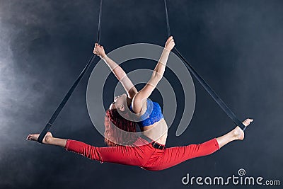 Female athletic, sexy and flexible aerial circus artist with redhead on aerial straps on black background Stock Photo