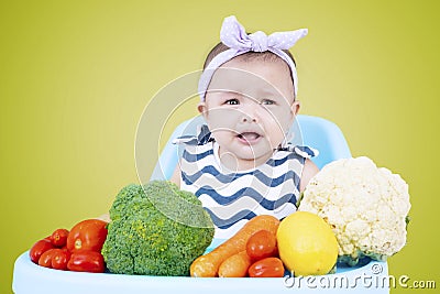 Female baby with vegetables on high chair Stock Photo