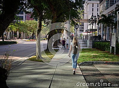 Female with backpack walking on empty sidewalk afternoon light back view Editorial Stock Photo