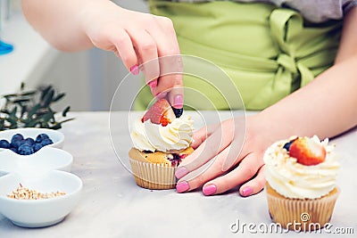 Female baker decorating tasty cupcake with berry. Pastry chef woman making creamy cakes Stock Photo