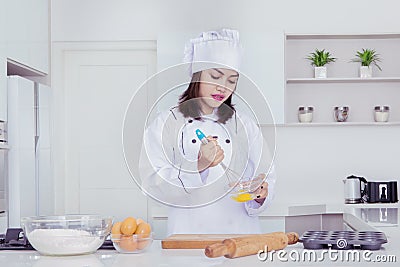 Female baker whisking eggs in a bowl to make cakes Stock Photo