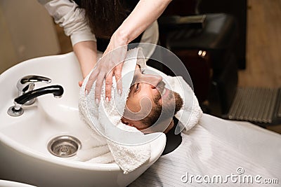 Female barber dries head of a man with soft towel Stock Photo