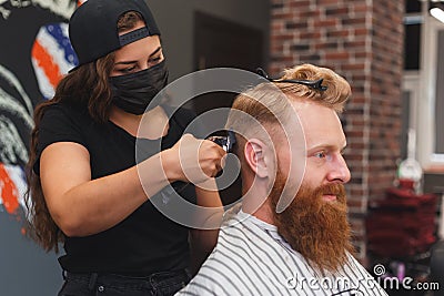 Female barber in mask cuts a man hairs with hair clipper. hairstyle during social distancing Stock Photo