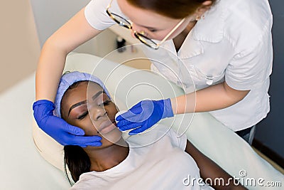 Female beautician doctor with patient in wellness center. Professional cosmetologist make procedure to beautiful African Stock Photo