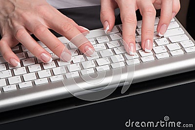 Female beautiful hands with classical French manicure are located over the computer keypad Stock Photo