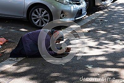 Female beggar with headscarf begs for money kneeling on a sidewalk Editorial Stock Photo