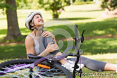 Female bicyclist with hurt leg sitting in park Stock Photo