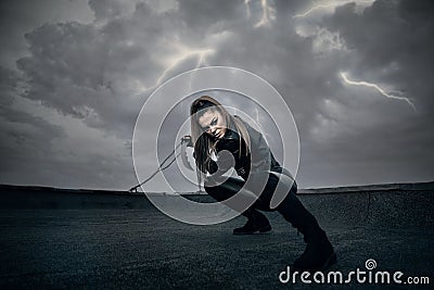 Female in black ninja assassin costume holding a sword, lighting in the sky Stock Photo