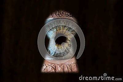 Female blue eye looking through the keyhole. Concept of voyeurism, curiosity, Stalker, surveillance and security Stock Photo