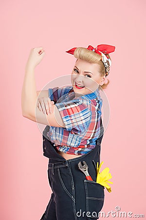 Female builder with red head scurf in blue denim with key in pocket and shows hand off isolated on pastel pink background Stock Photo