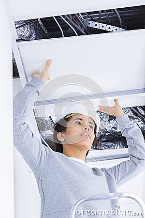 Female builder replacing suspended ceiling panel Stock Photo