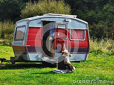 Female camper playing guitar near old small caravan in New Zealand Editorial Stock Photo