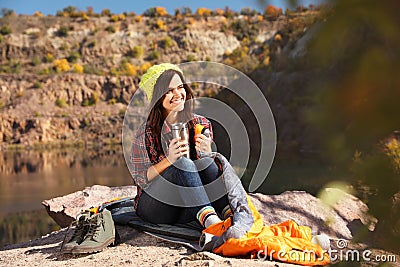 Female camper with thermos sitting on sleeping bag Stock Photo